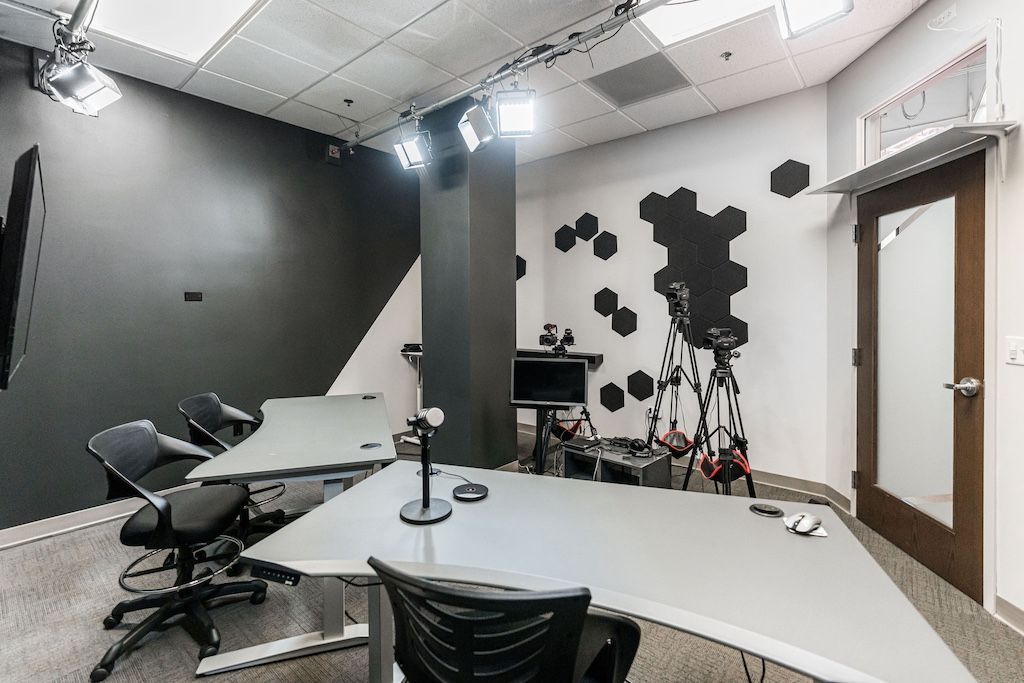 Studio interior with a large table, cameras on tripods, and black and white walls.