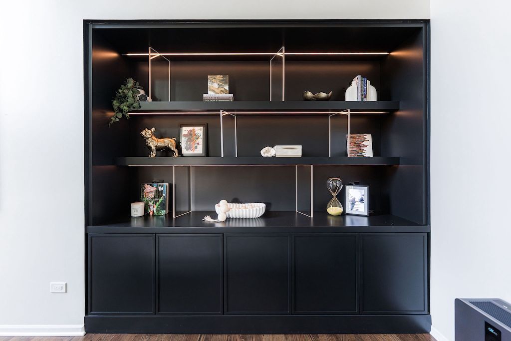 Black built-in cabinet with open shelves displaying decorative items and cabinet doors below, set against a white wall.