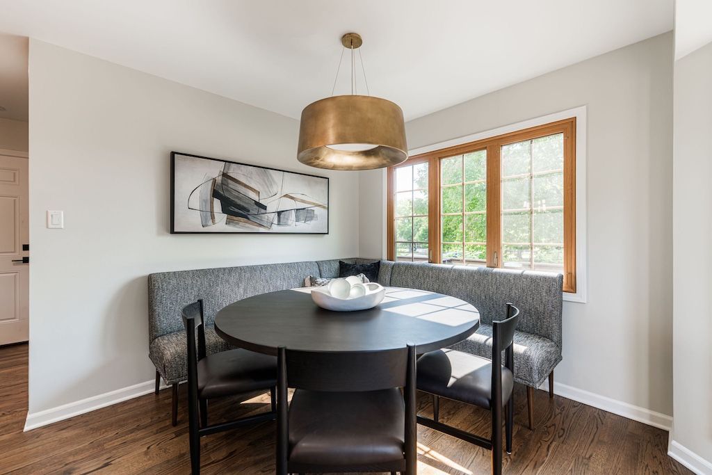 Dining area with a round black table, built-in bench, black chairs, and gold pendant light.