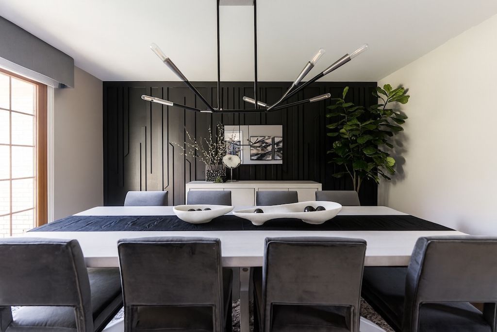 Modern dining room with a long white table, gray velvet chairs, and a black accent wall.
