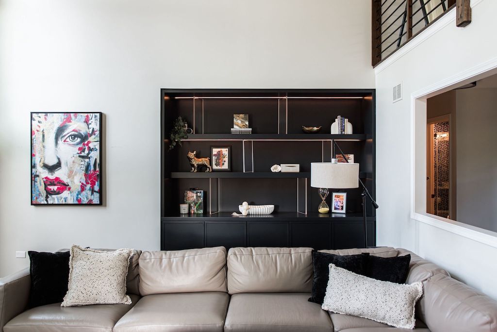 A modern living room with a black built-in bookshelf, sectional sofa, and abstract art.