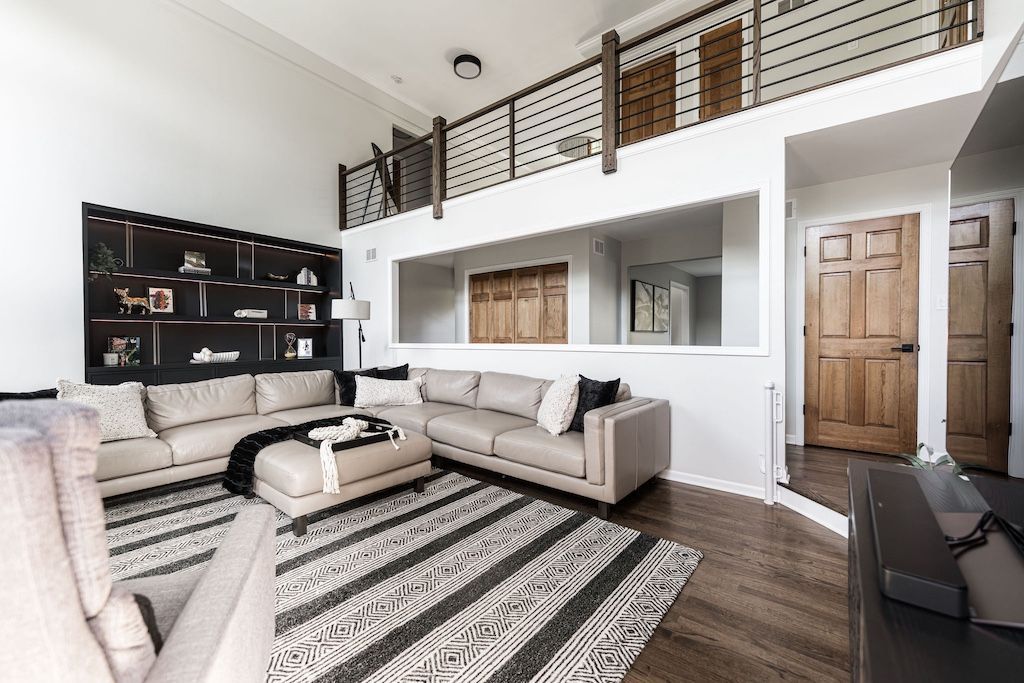 Living room with a loft, tan sectional, patterned rug, built-in shelving, and wooden door.