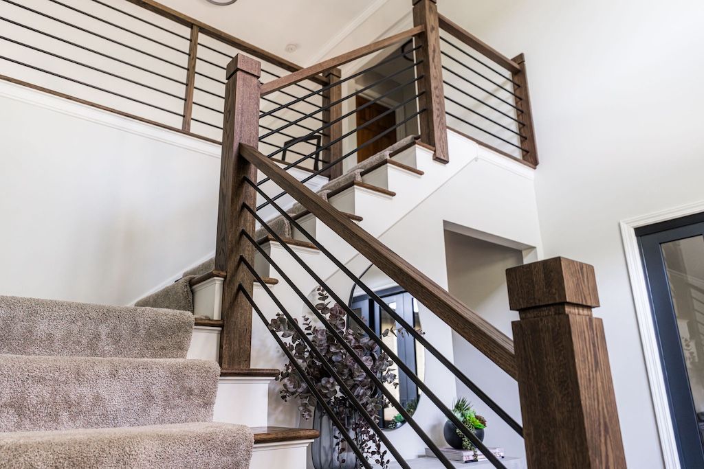 Staircase with wooden handrails, black metal railings, and carpeted steps.