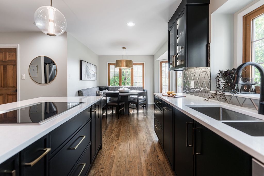 Modern kitchen with black cabinets, white countertops, and wood floors. Dining area visible.
