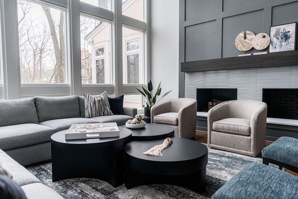 Modern living room with gray couch, black coffee tables, fireplace, and large windows.