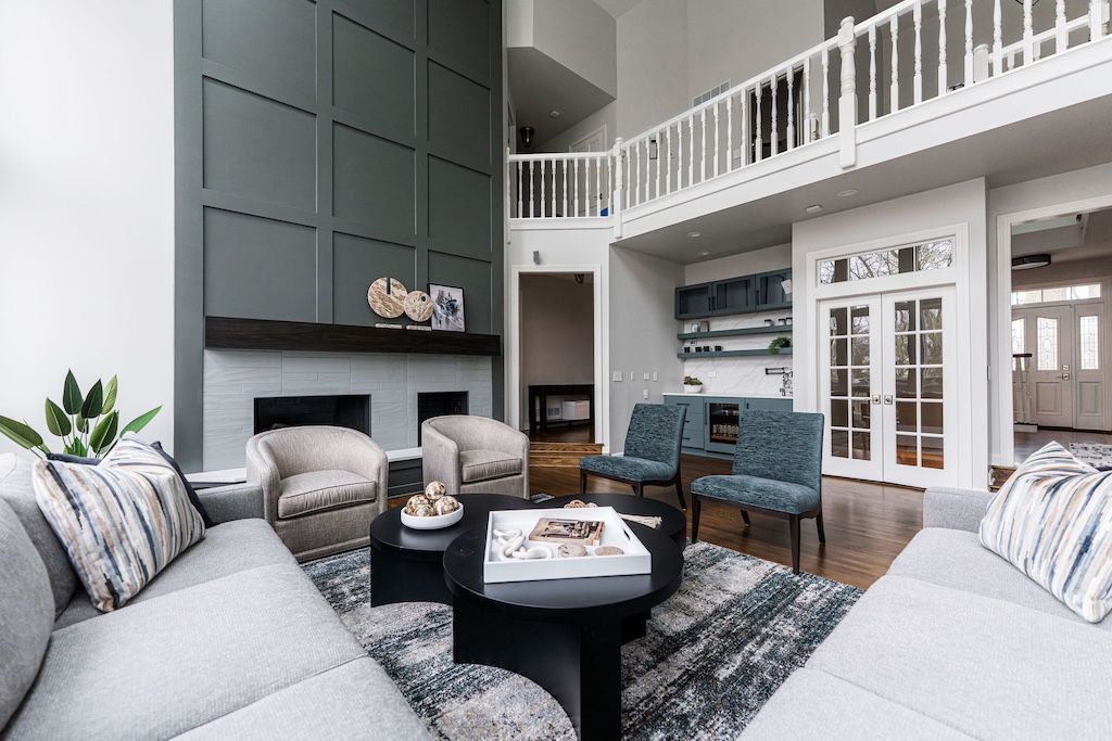 Spacious living room with gray sectional, fireplace, blue chairs, and a second-floor balcony.