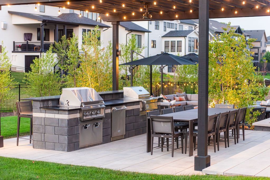 Outdoor kitchen with grill, dining table, and seating under a pergola.