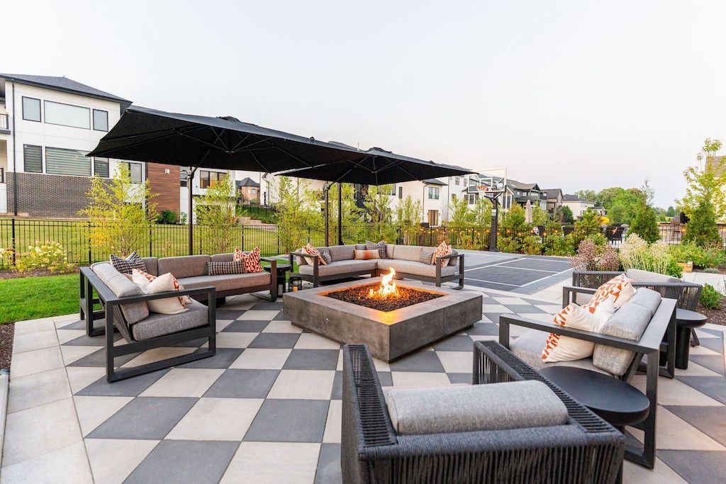 Outdoor patio with seating around a fire pit under a black pergola, checkered paving.