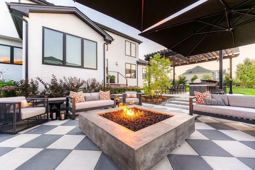Outdoor patio with fire pit, seating, and a checkered floor. White house in the background.