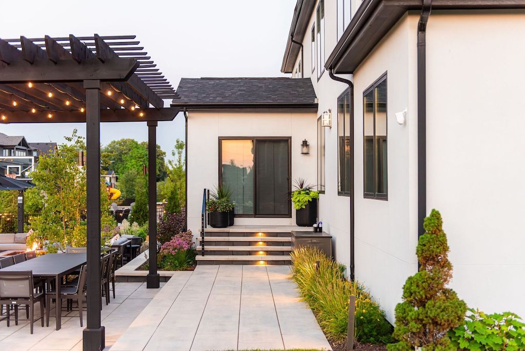 Patio with black pergola, dining set, and pathway leading to a white house with black trim.