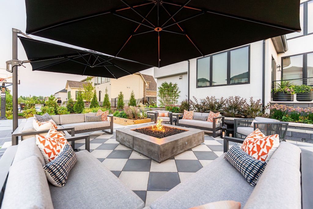 Outdoor seating area with fire pit, gray couches, black umbrella, and checkered patio.