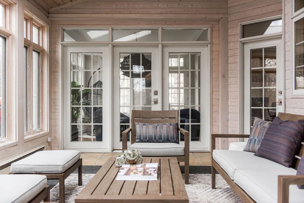 Sunroom with wooden furniture, glass doors, and light pink walls.