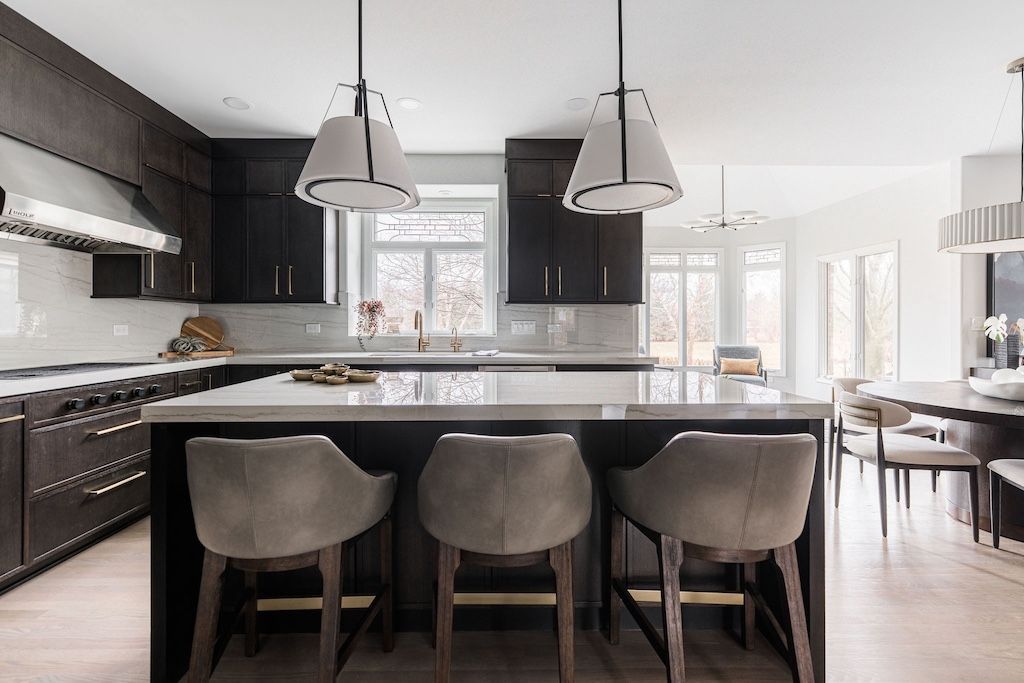 Modern kitchen with dark cabinets, white countertop island, and three gray bar stools.