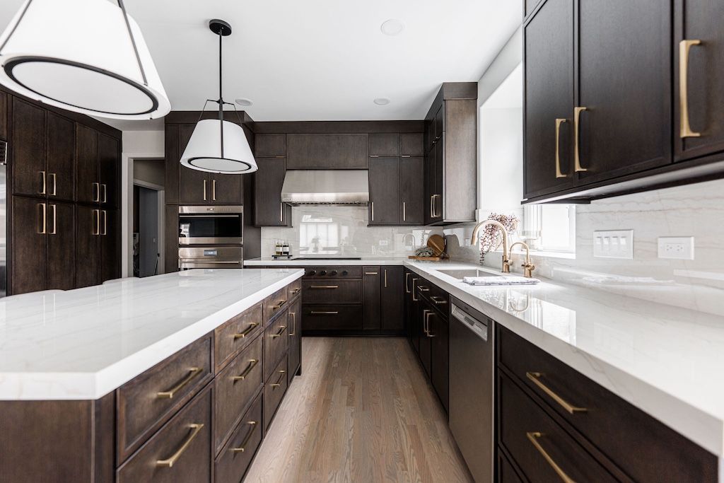 Modern kitchen with dark wood cabinets, white countertops, and stainless steel appliances.