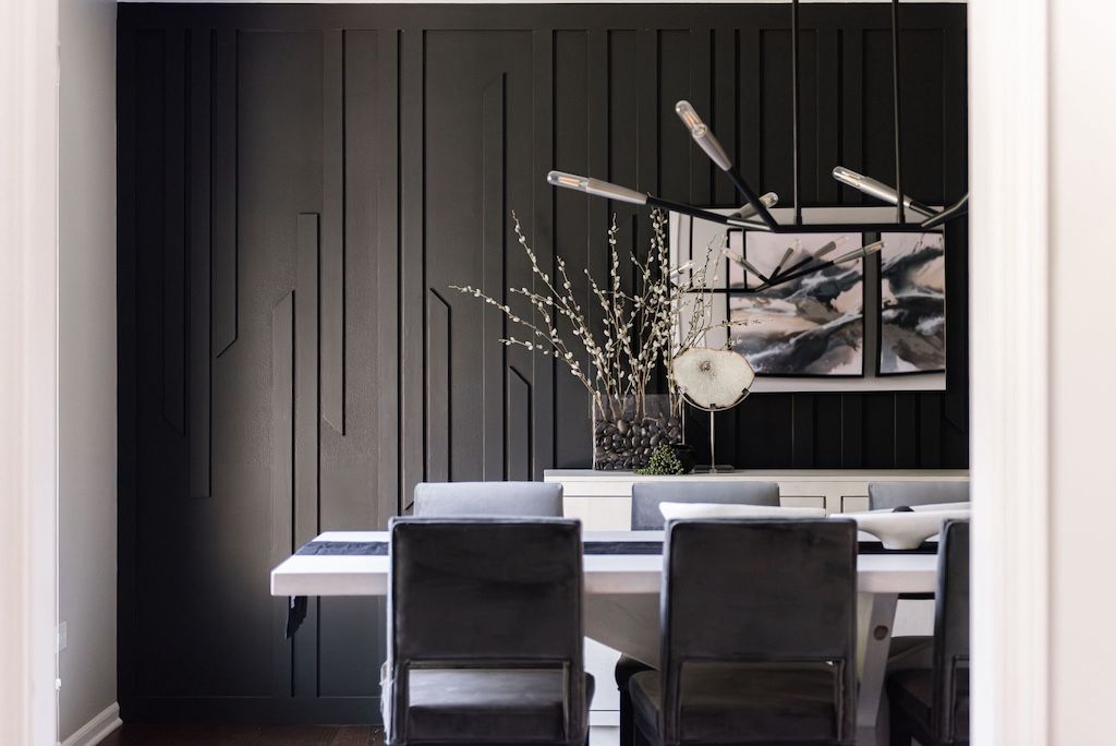 Dark dining room with black accent wall, white table, gray chairs, and modern light fixture.