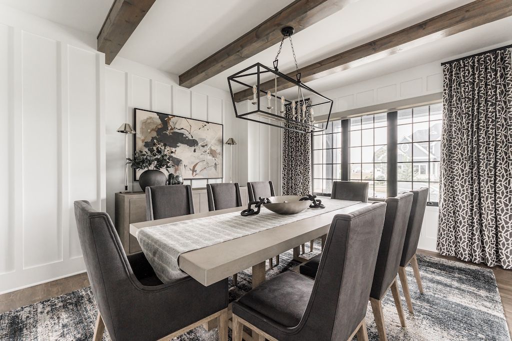 Elegant dining room with long table, gray chairs, wooden beams, and patterned curtains.