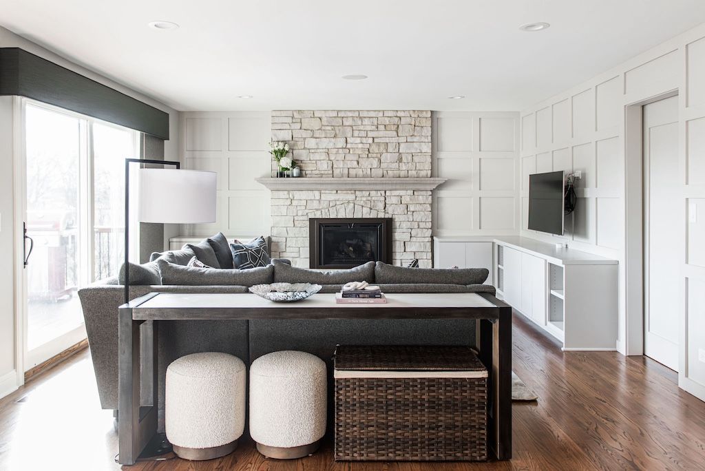 Living room with stone fireplace, gray sofa, white walls, wood floor, and side table.