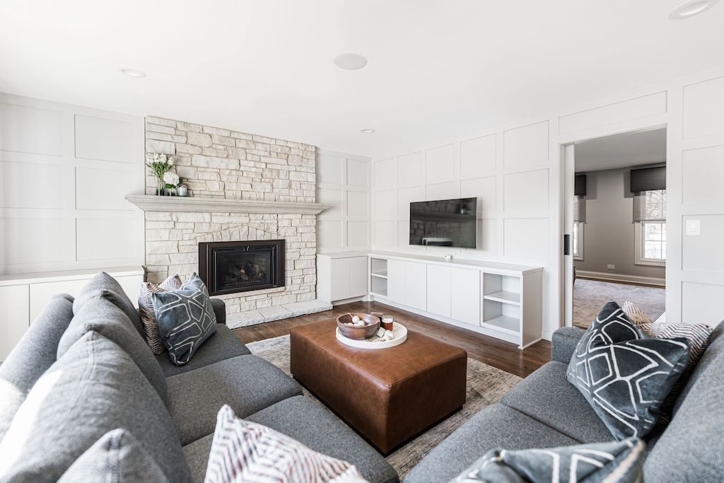 Living room with gray sectional, brick fireplace, leather ottoman, and TV.