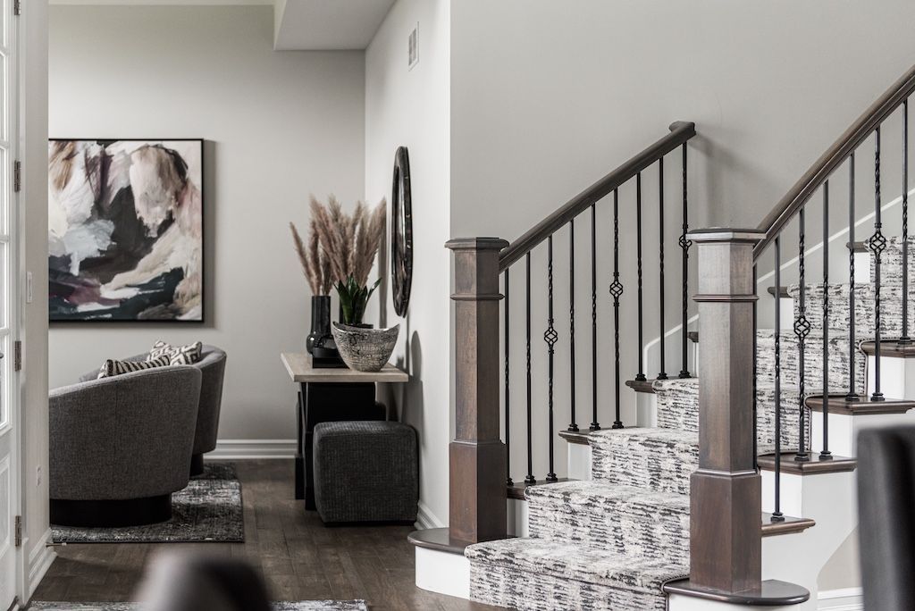 Hallway with staircase, art, and console table. Neutral tones with dark brown railing and patterned carpet on stairs.