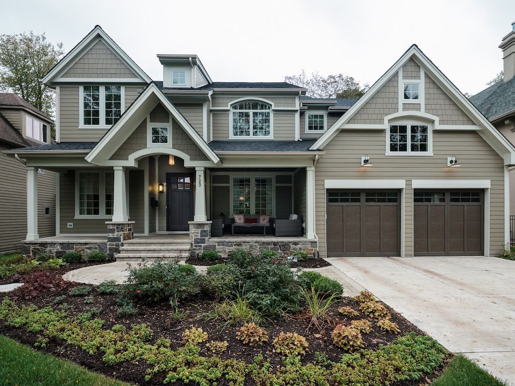 Two-story house with green siding, brown garage doors, and a landscaped front yard.