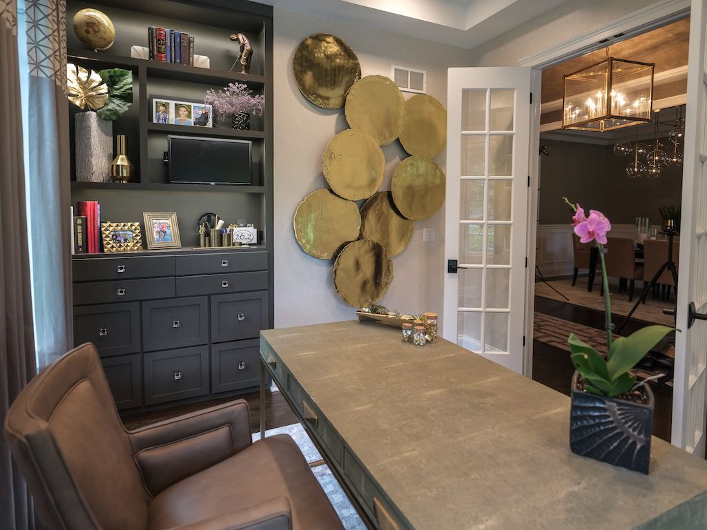 Home office with a desk, built-in shelves, gold wall decor, and French doors to a dining room.
