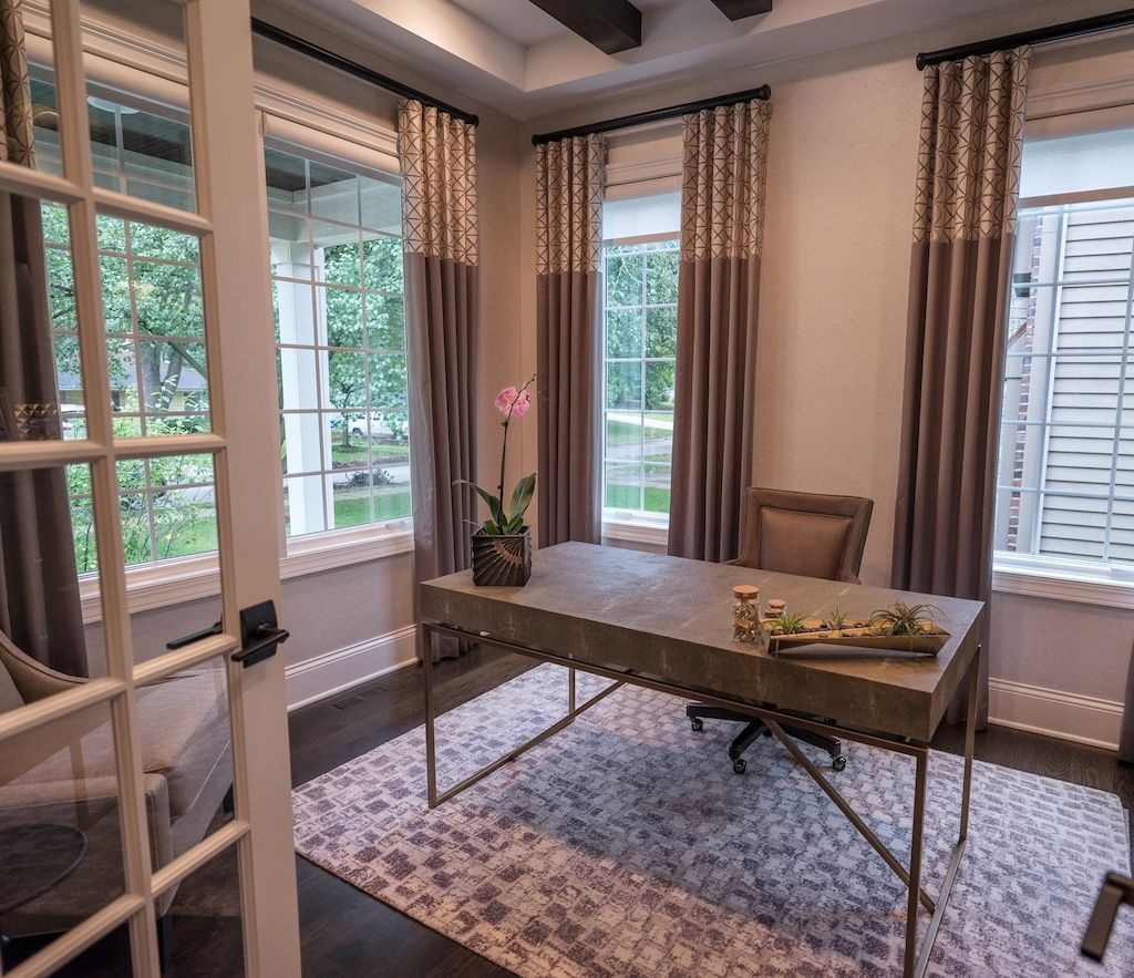 Home office with desk, windows, curtains, and orchid. Brown and beige tones, natural light.