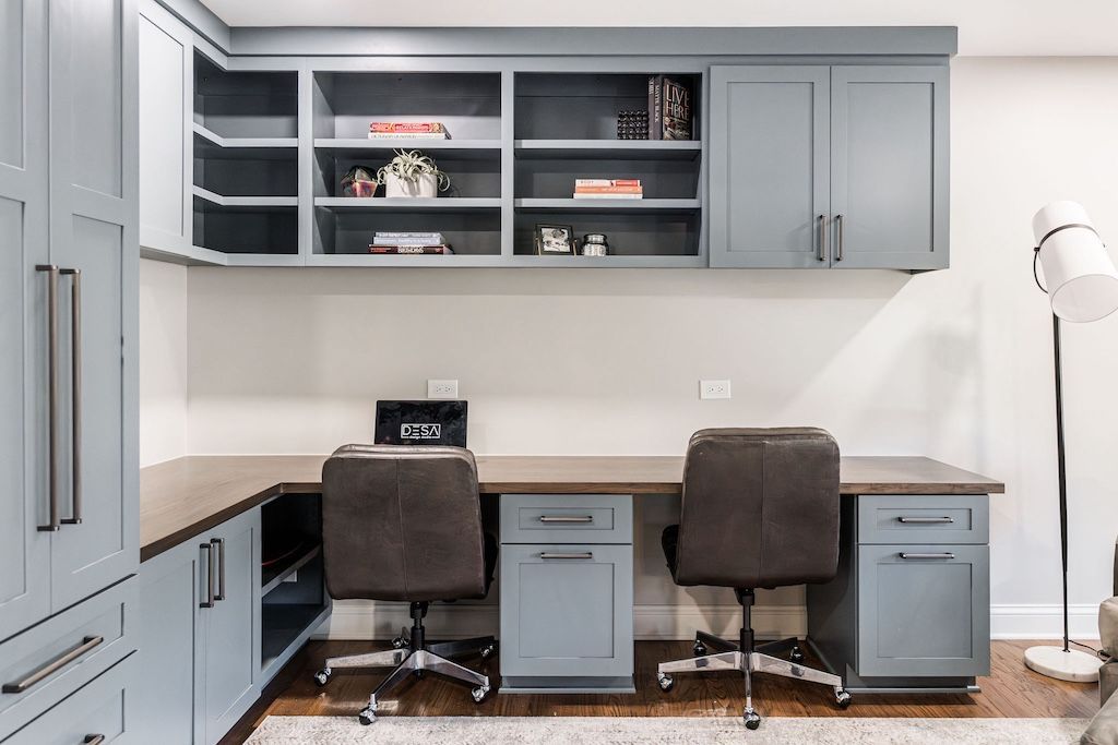 Home office with blue cabinetry, two desks, and brown chairs.