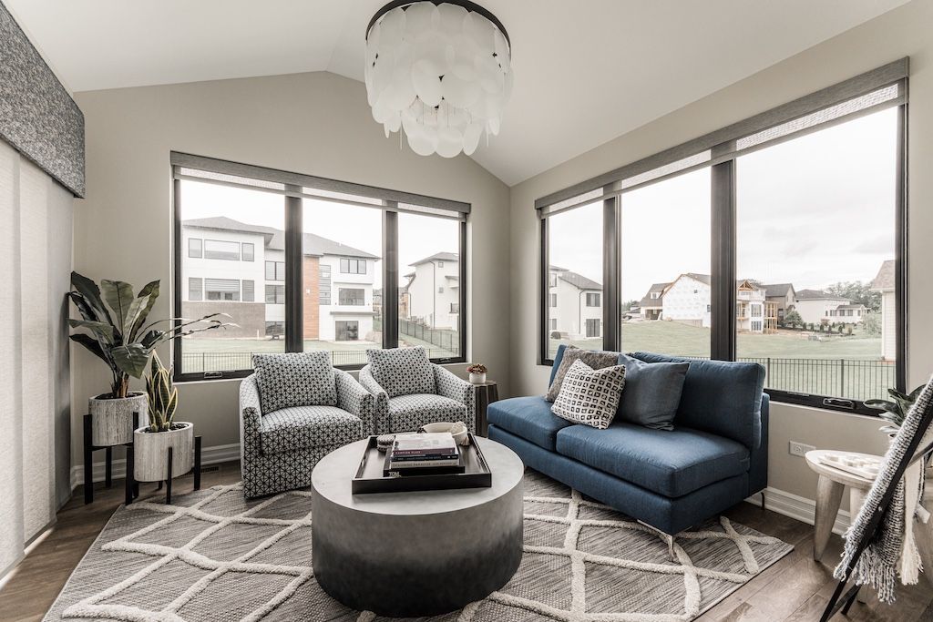 Sunroom with blue sofa, patterned chairs, round ottoman, and large windows.