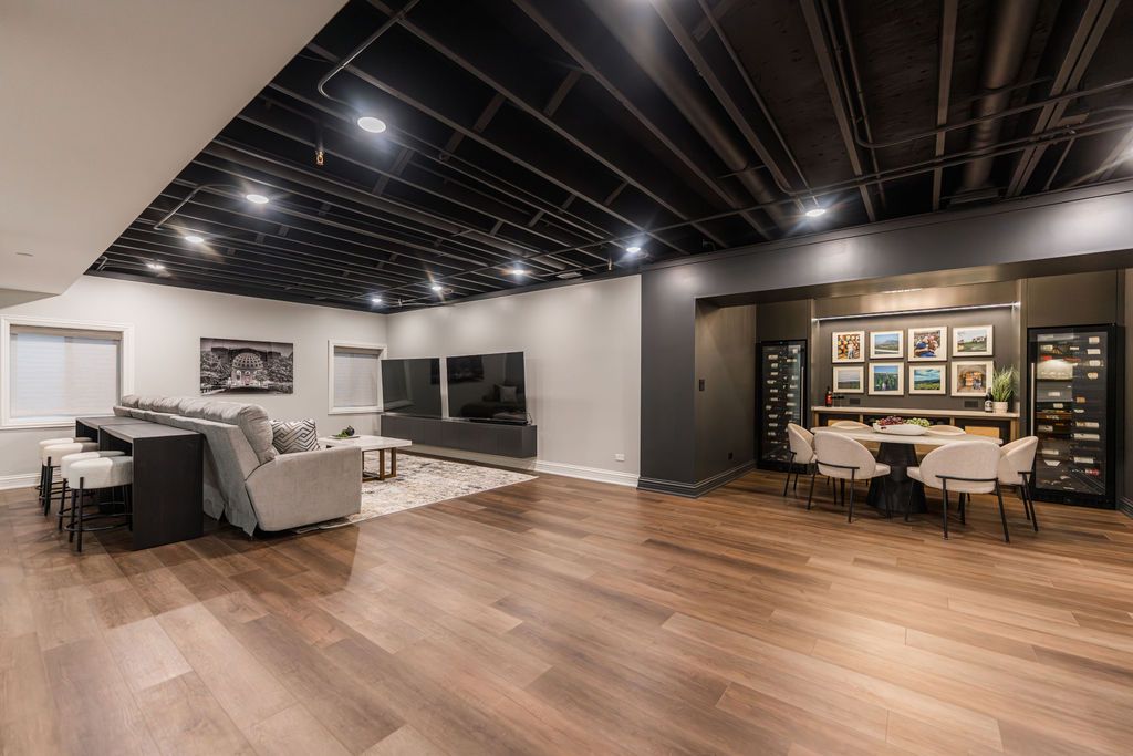 A spacious, modern basement with wood floors, a black exposed ceiling, a sectional sofa, a television, and a dining area.