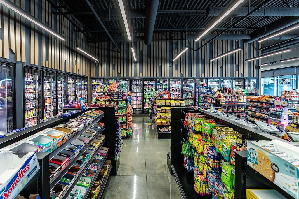 Grocery store interior, displaying refrigerated and shelf-stocked food items, with overhead lighting.