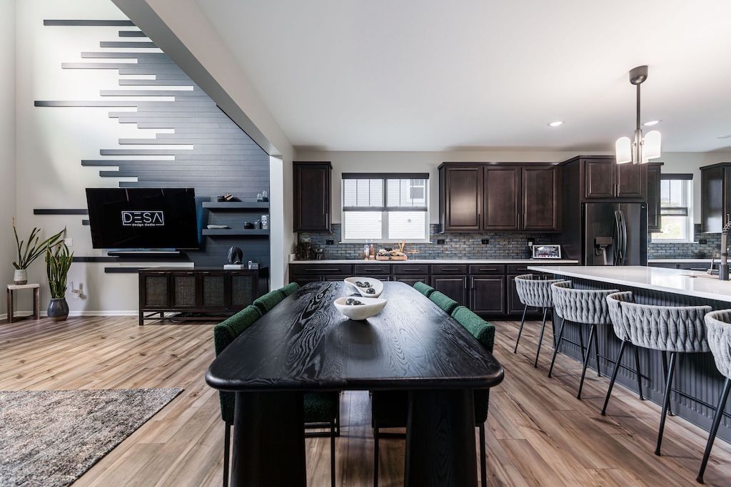 Modern kitchen and dining room with a long black table, dark cabinets, and wood flooring.