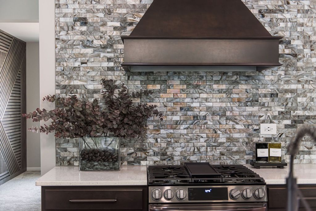 Kitchen with gas range, mosaic backsplash, dark wood cabinets, and bronze range hood.