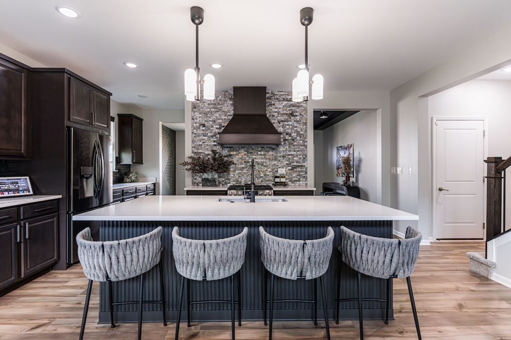 Modern kitchen with island, dark cabinets, and four gray woven bar stools.
