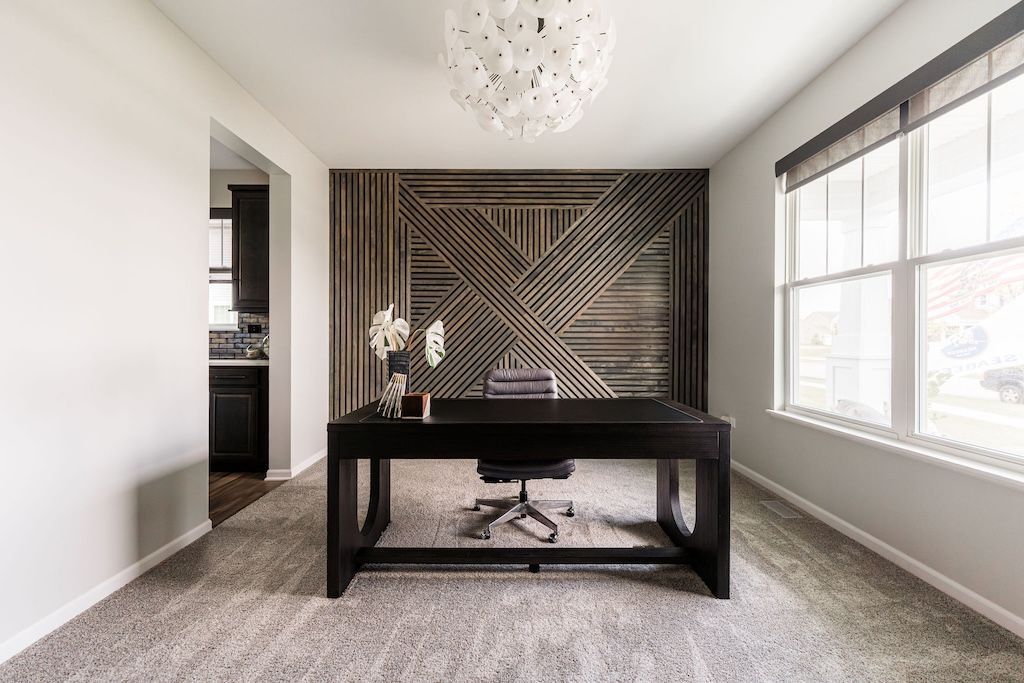 Home office with wooden accent wall, black desk, window, and gray carpet.