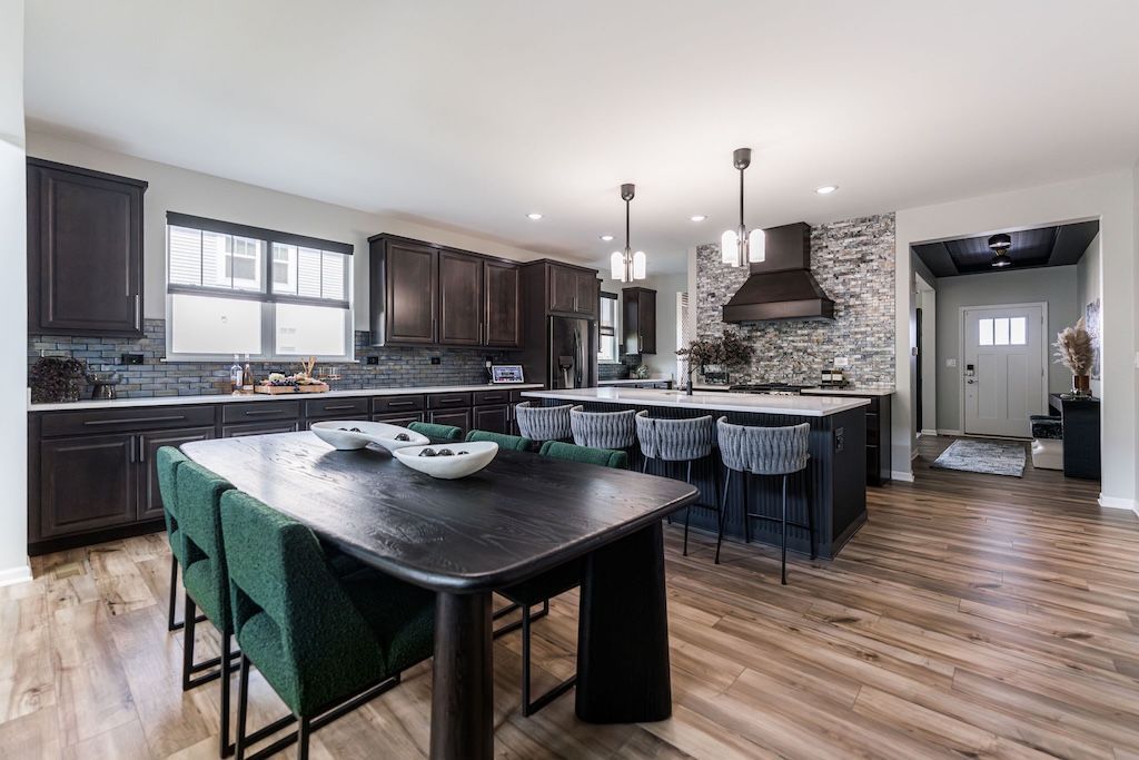 Open-concept kitchen with dark cabinets, a large island, and a dining table with green chairs.