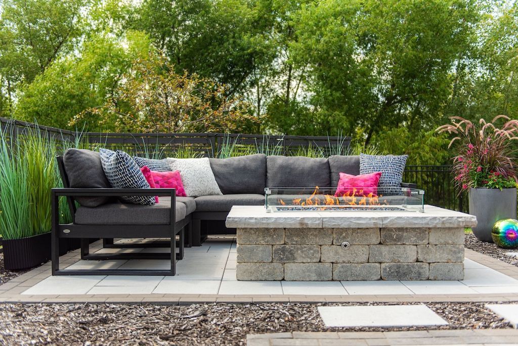 Outdoor patio with sectional sofa, fire pit, and potted plants.