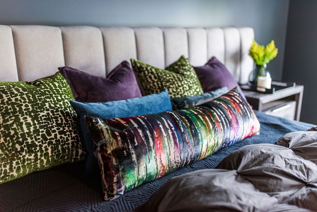 Bedroom with assorted throw pillows on a bed, and a nightstand with flowers.