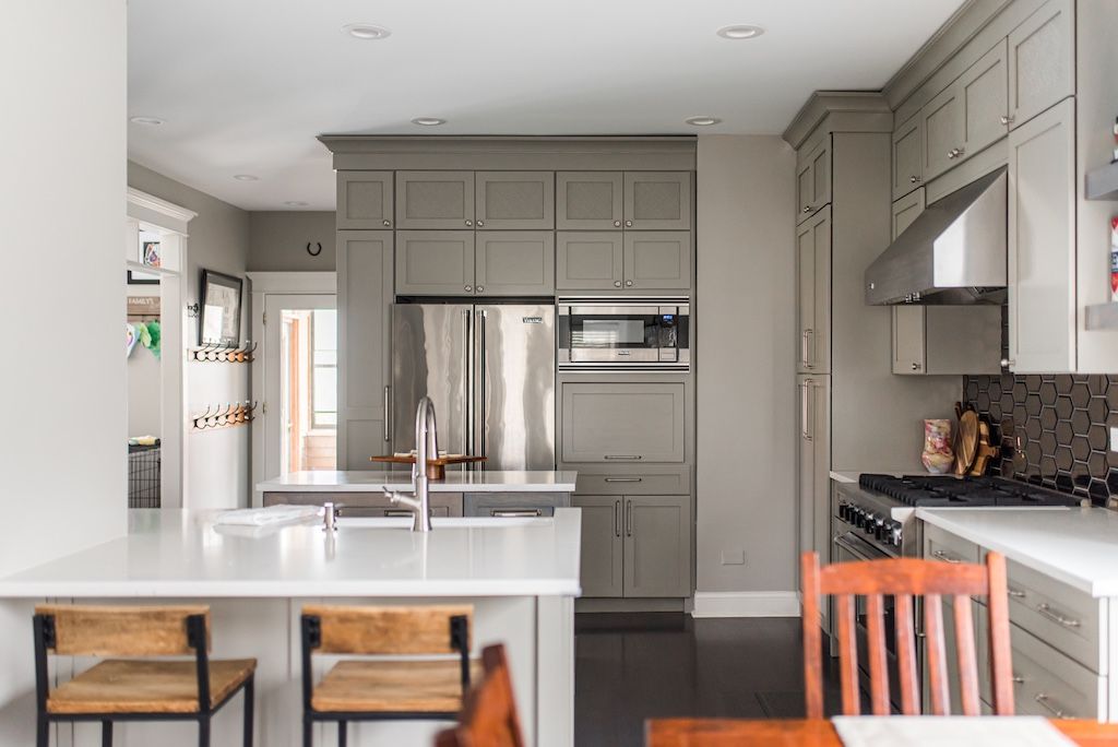 Gray kitchen with white island, stainless steel appliances, dark wood floors, and wooden chairs.