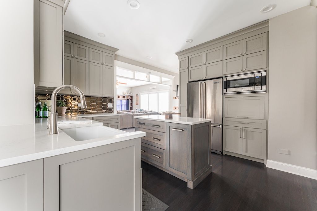 Modern gray kitchen with island, cabinets, stainless steel appliances, white countertops, and dark wood floors.