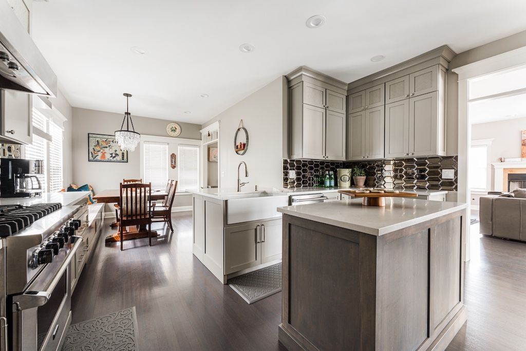 Spacious gray and white kitchen with two islands, a dining table, stainless steel appliances, and dark hardwood floors.