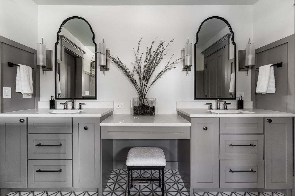 Gray and white bathroom with two sinks, mirrors, and a vanity, accented by decorative floral branches.