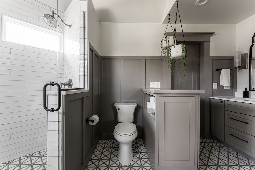 Gray and white bathroom with shower, toilet, and vanity; potted plants hang from ceiling.