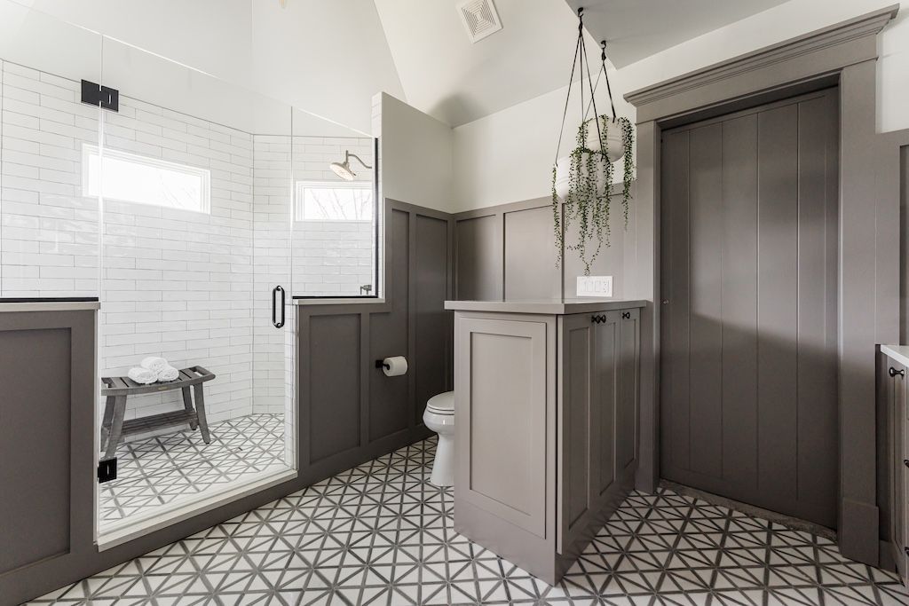 Gray and white bathroom with a glass shower, patterned tile floor, and a hanging plant.