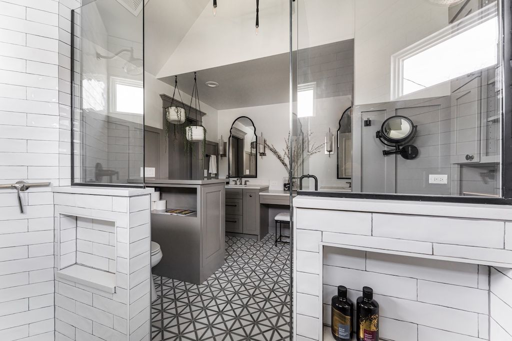 Modern bathroom with gray and white tile, glass shower, patterned floor, vanity with mirrors.