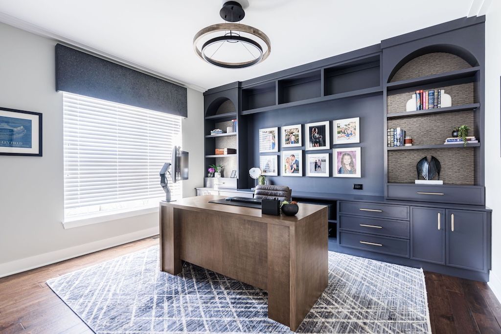 Home office with dark blue built-ins, wooden desk, and patterned rug.