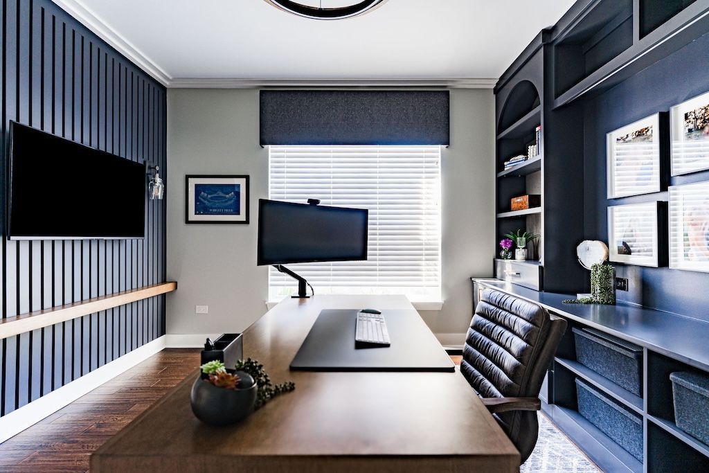 Modern home office with dark blue accent wall, wooden desk, and built-in shelving.