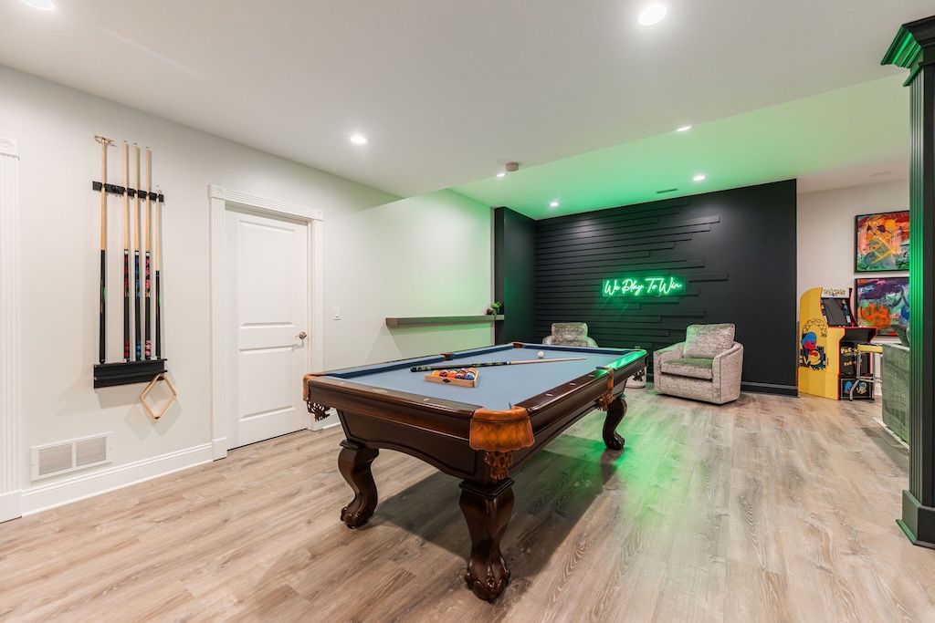 Pool table in a game room with wooden floors, black accent wall, and neon sign.