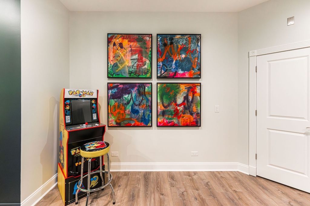 Arcade game next to colorful abstract art on a pale wall, in a room with a closed door.