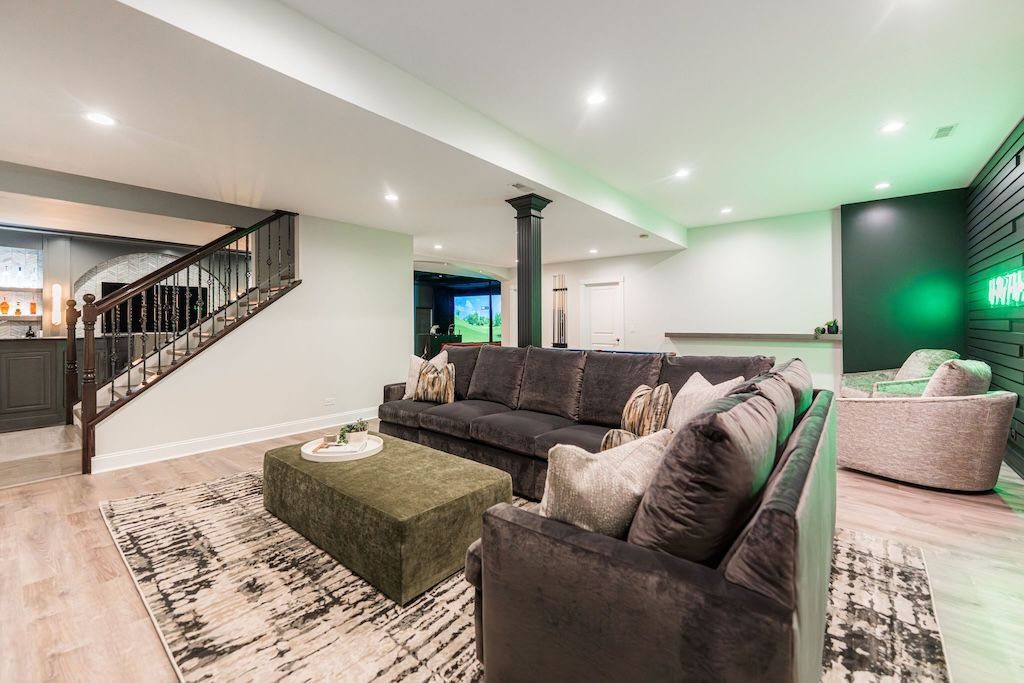 Modern living room with dark gray sofa, green ottoman, and staircase.