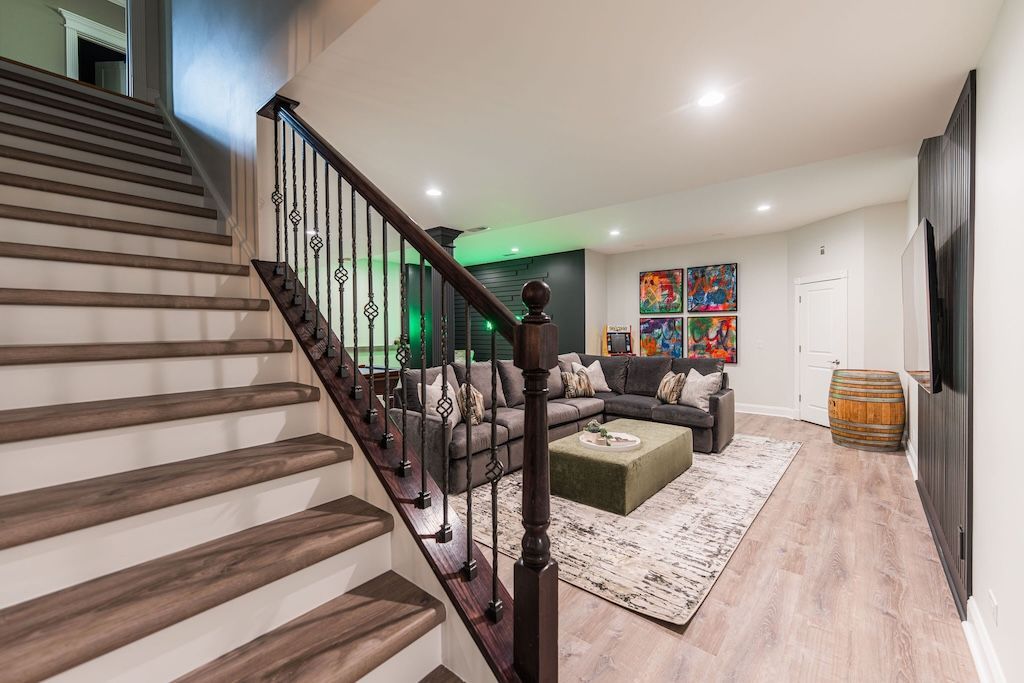 Wooden staircase leading to a modern basement living area with a sectional sofa and colorful art.